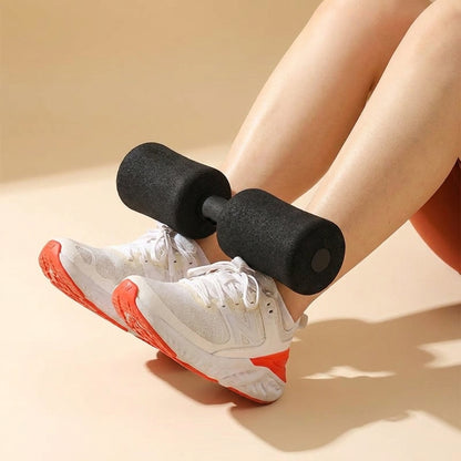 A person's legs resting on a beige floor with a pair of white and orange athletic sneakers, using a small black foam dumbbell as a prop.